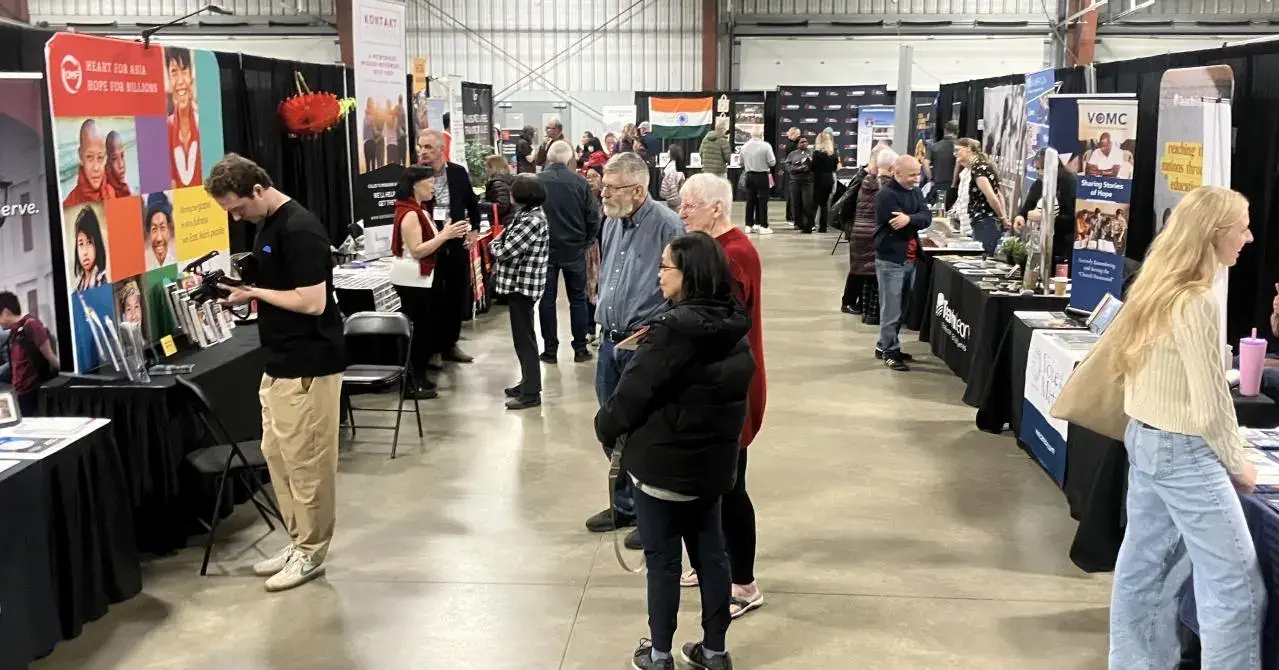 A diverse crowd of conference attendees are visiting a number of exhibitor hall booths in a brightly coloured room